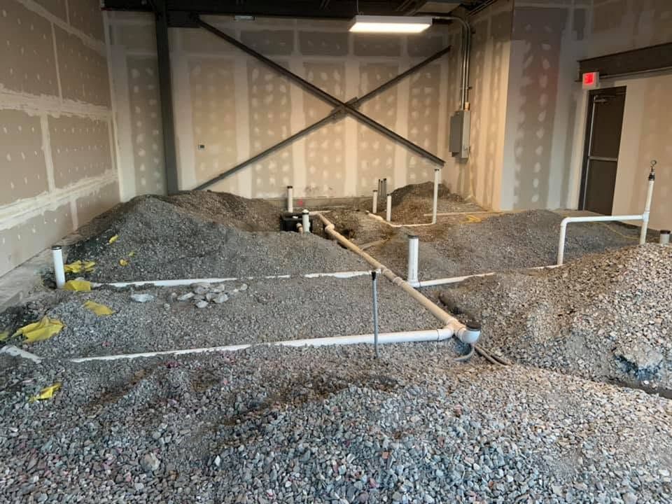 White PVC drain lines and cleanout risers laid across a gravel bed inside a building